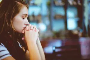 A young woman sitting down with her eyes closed and her hands folded.