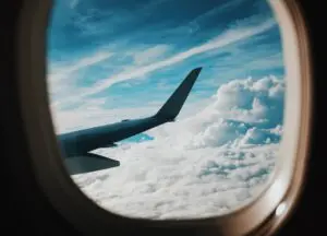 A view of clouds and sky below from the window seat of a commercial airplane.