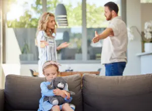 Kid feeling upset while parents argue in room. Couple arguing around child. Impact of family conflicts or divorce. Sad girl hugging teddy bear