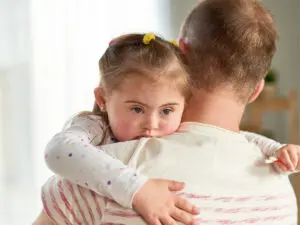 Young girl with down syndrome hugging her dad who is holding her in his arms.