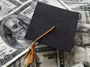 A graduation cap on a pile of hundred dollar bills.
