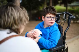 Disabled boy in a wheelchair with a soccer ball while enjoying the outdoors playing with his mother in the park. Disability concept.