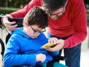 A special needs child in a wheelchair being given a phone from his father.