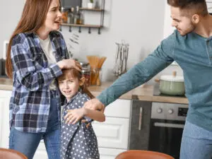 A woman holding her son defensively against the father who is grabbing the son by the arm in anger.