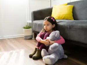 A young girl holding a stuffed animal on the ground.