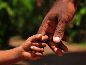 Close-up of a child holding an adult's hand outdoors, symbolizing trust, protection, and parent-child connection
