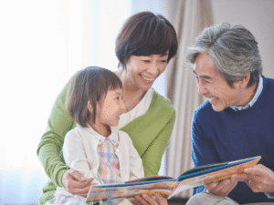 A young girl with her grandparents reading a book together.