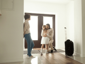 A toddler hugging a parent who is leaving with a suitcase, illustrating the transitions and exchanges related to co-parenting schedules toddlers.