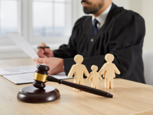 A judge sits at a desk reviewing documents while a gavel rests in the foreground beside wooden figures representing a family of three. The image visually represents child custody decisions, particularly those involving family structure and the court’s role in determining arrangements that serve the best interests of a child, including cases involving special needs and caregiving responsibilities.