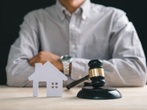 Close-up of a judge’s gavel beside a small house model with a person seated in the background, representing legal decisions about marital home occupancy during a divorce in San Diego.