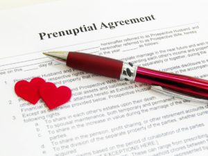 Close-up of a prenuptial agreement document with a pen and small red heart decorations, symbolizing marriage, financial planning, and legal agreements between partners.