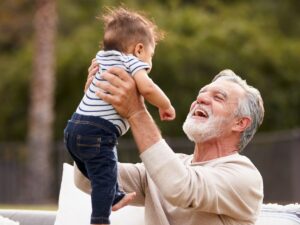 An older grey man holding a baby up in the air.