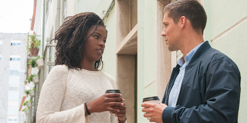 a man and woman each holding a cup of coffee looking at each other