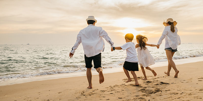 two adults and two children holding hands walking on the beach